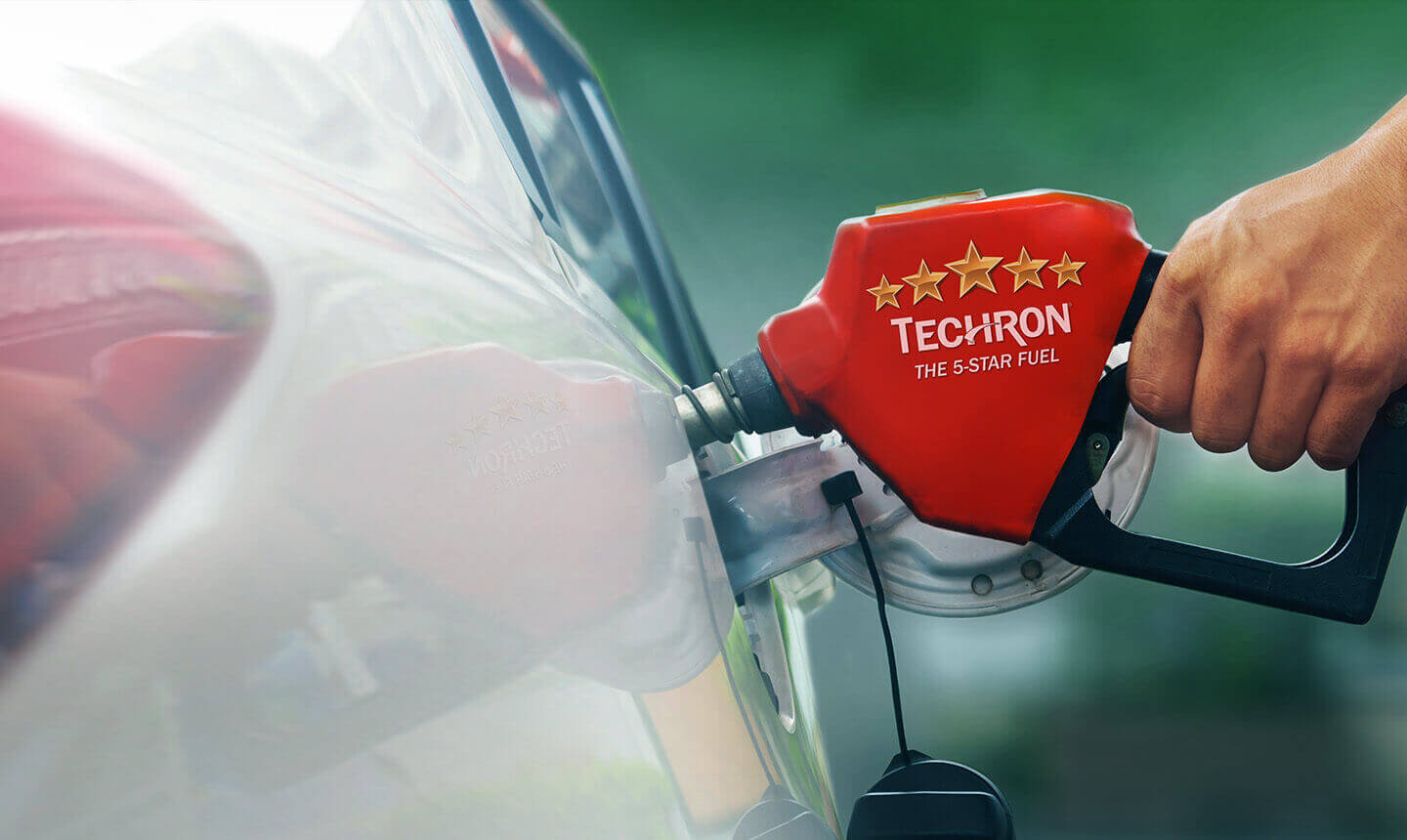 Hand holding a red pump nozzle refuelling a car